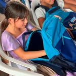 Beneficiaria con curiosidad y alegria abre el kit escolar entregado durante la jornada