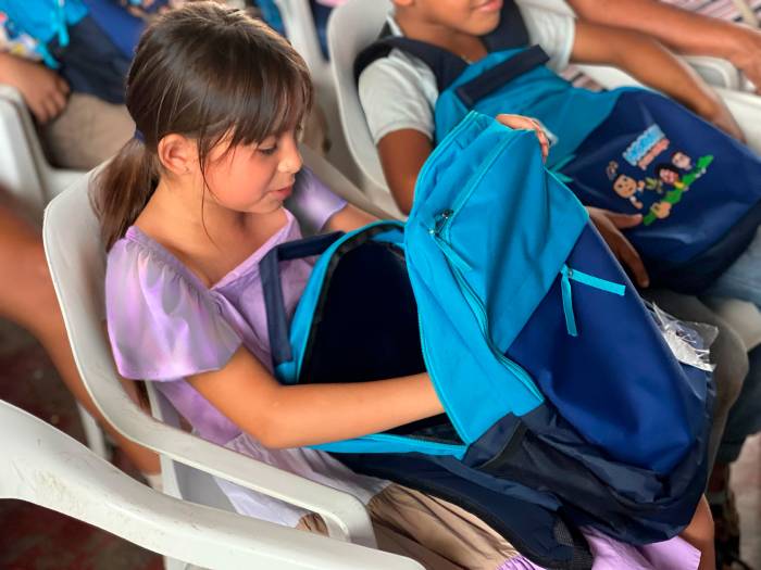 Beneficiaria con curiosidad y alegria abre el kit escolar entregado durante la jornada