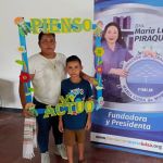 Niño con su acompañante posan dentro de un marco decorativo sobre la conciencia ambiental junto al pendón de la Dra. María Luisa.
