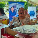 Beneficiaria riendo con un recipiente de vidrio en manos, mostrando su alegría por los artículos de repostería recibidos.