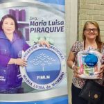 Beneficiarios muestran sus kits de aseo al lado del pendón de la Dra. María Luisa.