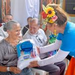 Mujer adulta mayor recibe con alegría en su rostro un kit escolar de parte de la voluntaria.