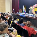 Una voluntaria y mujer adulta mayor realizan una actividad desde tarima para los participantes