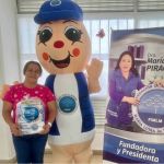 Beneficiaria posa junto a Hormy y el pendón de la Dra. María Luisa después de la entrega de kits de aseo.