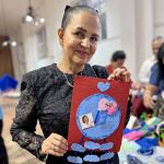 Con una obra de arte en sus manos, una mujer muestra con alegría la carta con figuras de papel y fotografías sobre el cariño y admiración hacia la Dra. María Luisa