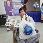 Beneficiaria posa en una foto institucional con el mercado recibido y el aprendizaje de los valores en el taller