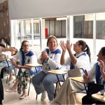 De pie, una voluntaria irradia una alegría absoluta y contagiosa, extendiendo sus manos no solo para compartir un mensaje, sino para abrazar con el alma al equipo.