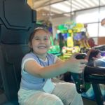 Una niña se muestra sonriente al divertirse en los simuladores de conducción