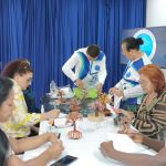 Estudiantes y voluntarios profesores trabajan en una mesa alargada durante el taller formativo práctico