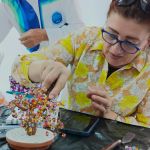 Estudiante trabaja en la copa de un Árbol artesanal, acomodando pequeñas piedras multicolor en sus ramas con su mirada fija en los detalles