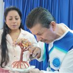 Voluntario concentrado utiliza herramienta para moldear la base texturizada de un Árbol artesanal y enseña esta práctica a nuestra estudiante