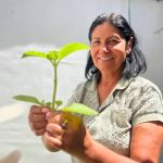 Una mujer sostiene con una sonrisa una planta que fue cosechada de la huerta